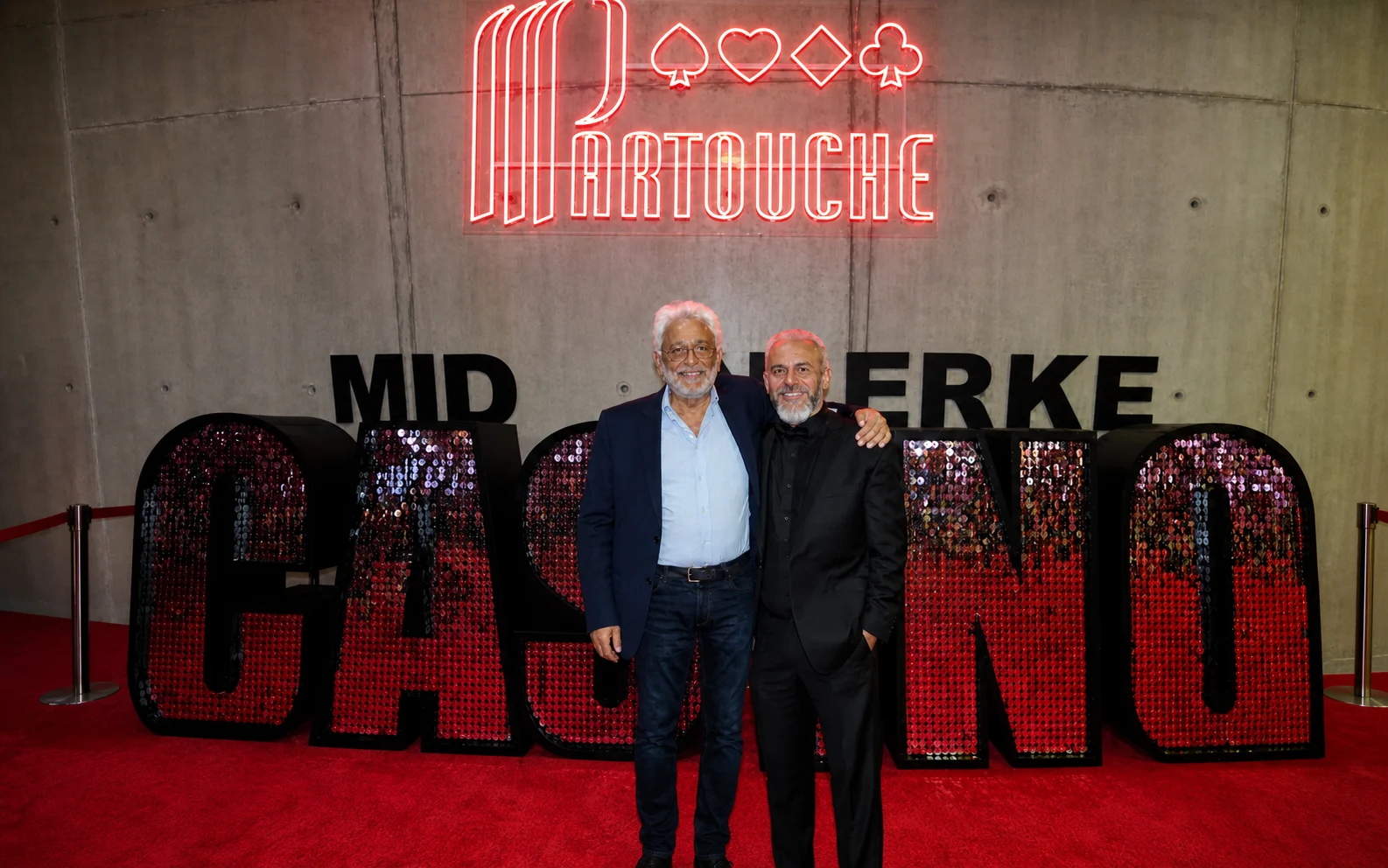 Christophe Porquet and a Groupe Partouche representative beneath the illuminated Partouche sign at a venue event.